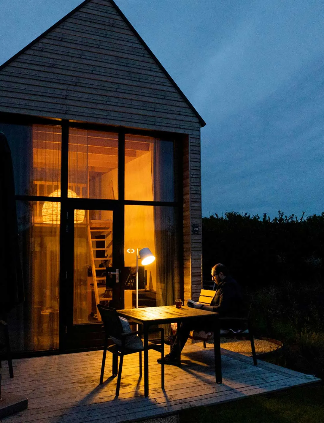 Mann liest im warmen Licht von seinem Holzhaus