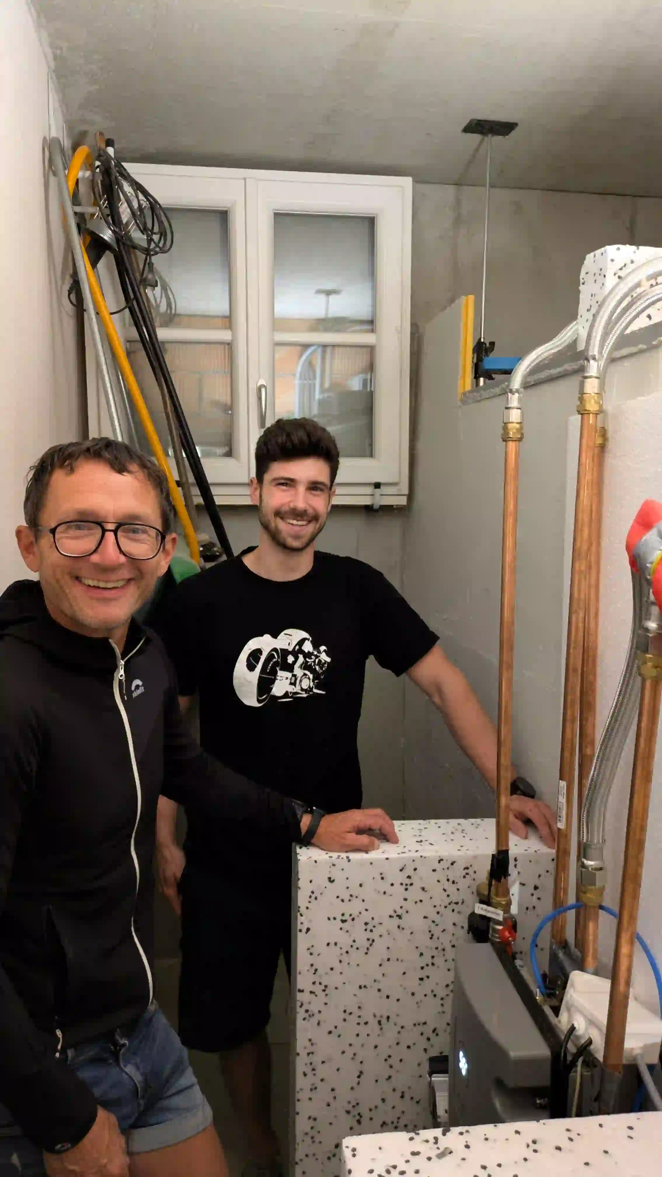 Zwei Männer stehen im Heizungskeller neben einem isolierten Wärmespeicher mit Kupferrohren