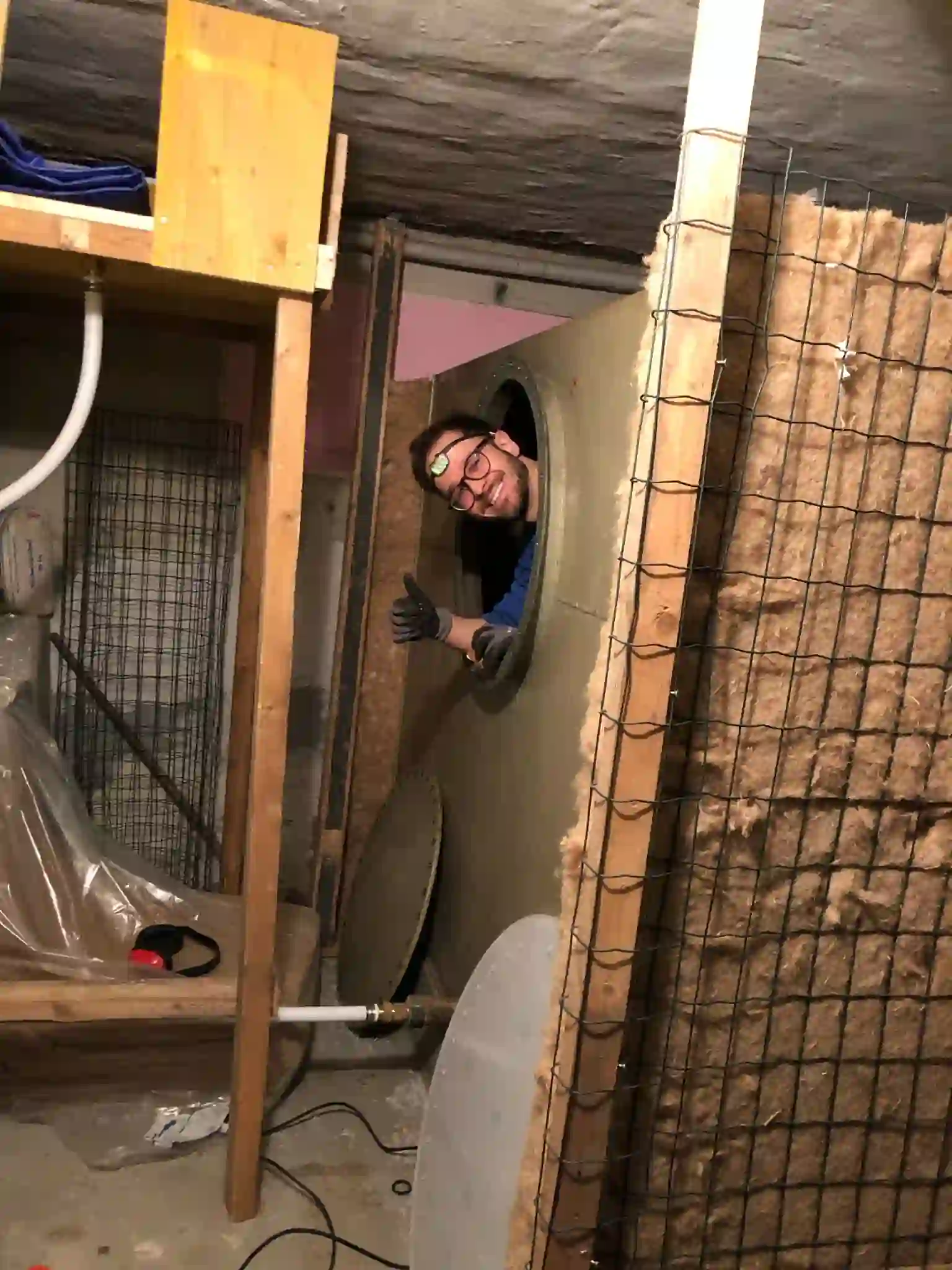 Mann mit Brille und Arbeitshandschuhen schaut lächelnd durch die runde Öffnung eines Öltanks im Keller