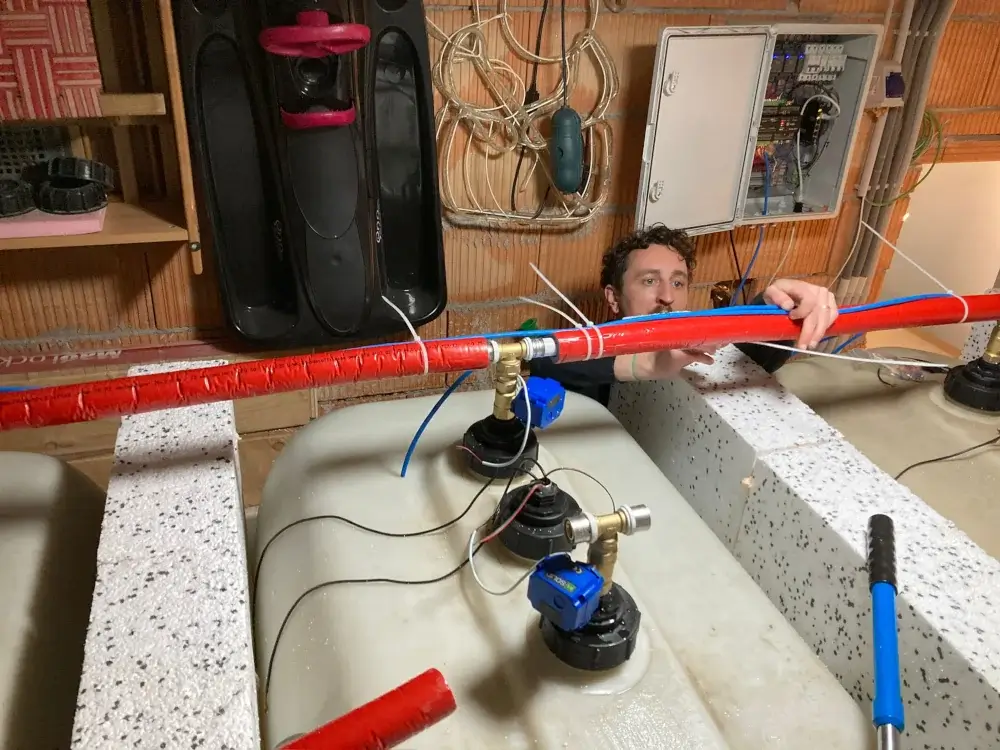 Mann arbeitet an roten und blauen Rohren, die mit isolierten Tanks im Keller verbunden sind