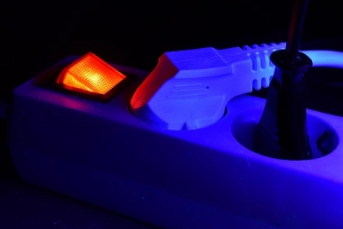 Steckdosenleiste mit leuchtendem orangefarbenem Schalter und eingestecktem weißem Stecker